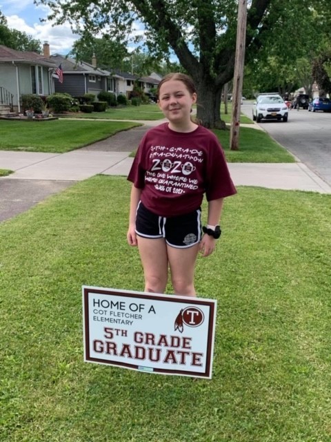Student posing near 5th grade graduate sign
